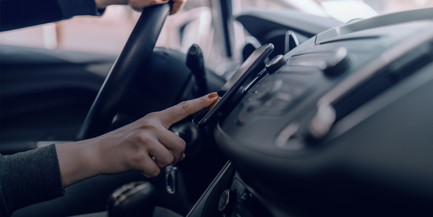 Une femme au volant de sa voiture appuie sur son téléphone pour suivre sa geolocalisation